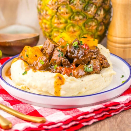 Slow cooker sweet chili pineapple steak tips plated on mashed potatoes with caramelized pineapple and garnish