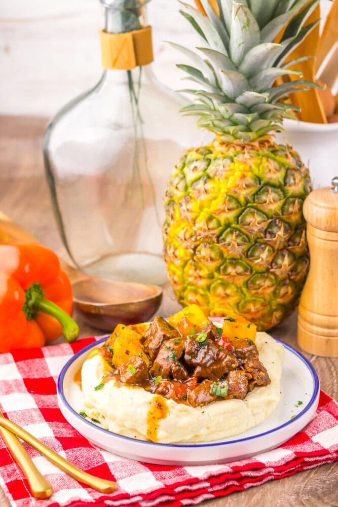 Slow cooker sweet chili pineapple steak tips served over mashed potatoes with fresh pineapple and vegetables in a styled kitchen setting