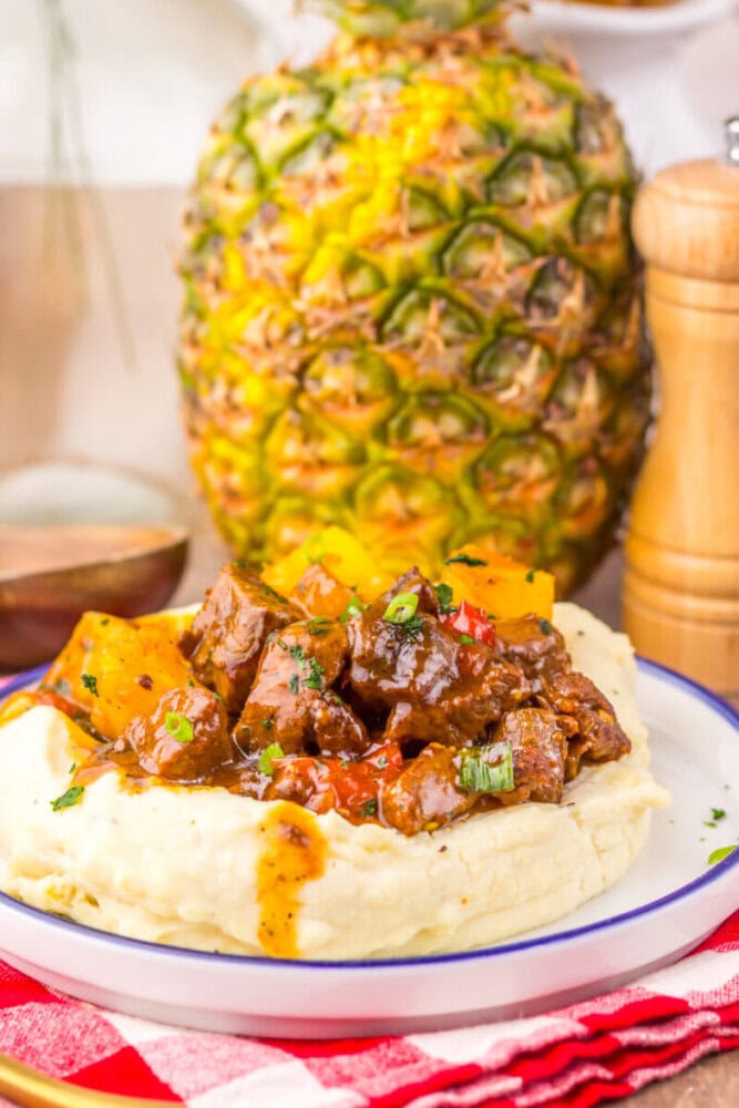 Slow cooker sweet chili pineapple steak tips served on creamy mashed potatoes with fresh garnish and whole pineapple