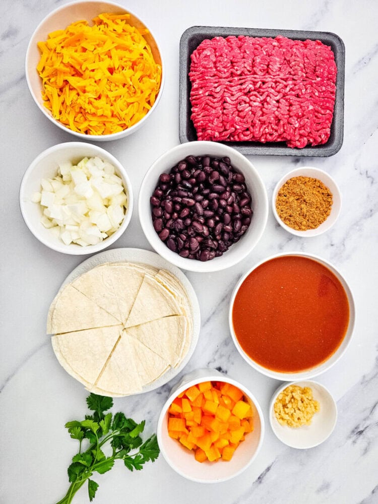 Beef enchiladas skillet ingredients laid out - cheese, ground beef, tortillas, beans, peppers, sauce and seasonings