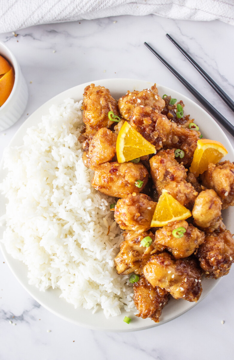 Orange chicken with rice plated on white dish with orange garnish and green onions