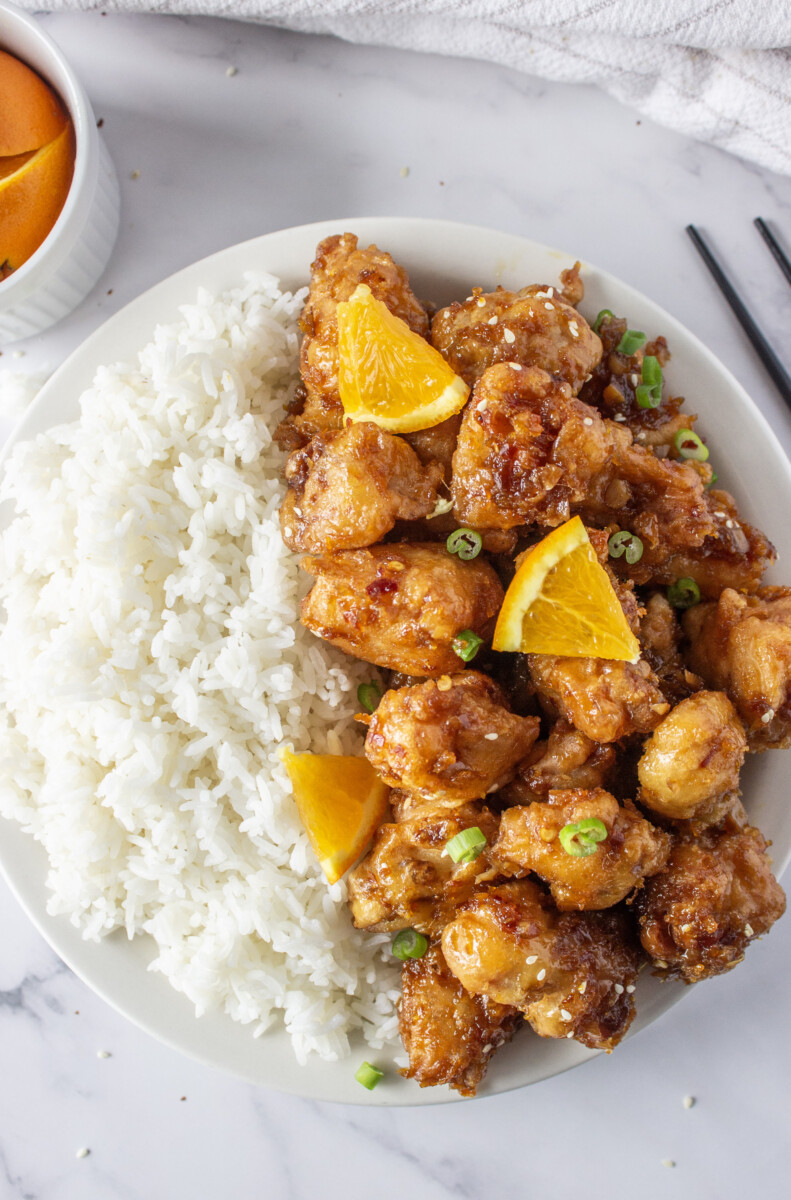 Orange chicken with white rice and orange garnish on white plate