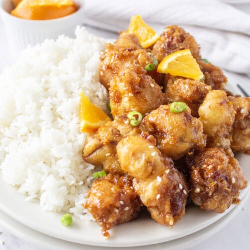 Orange chicken with sesame seeds and orange garnish served with white rice