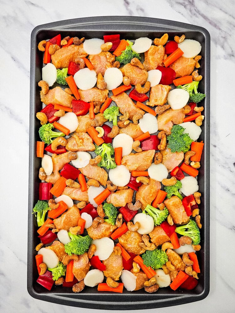 Sheet pan cashew chicken with broccoli, bell peppers, carrots and cashews on black baking tray