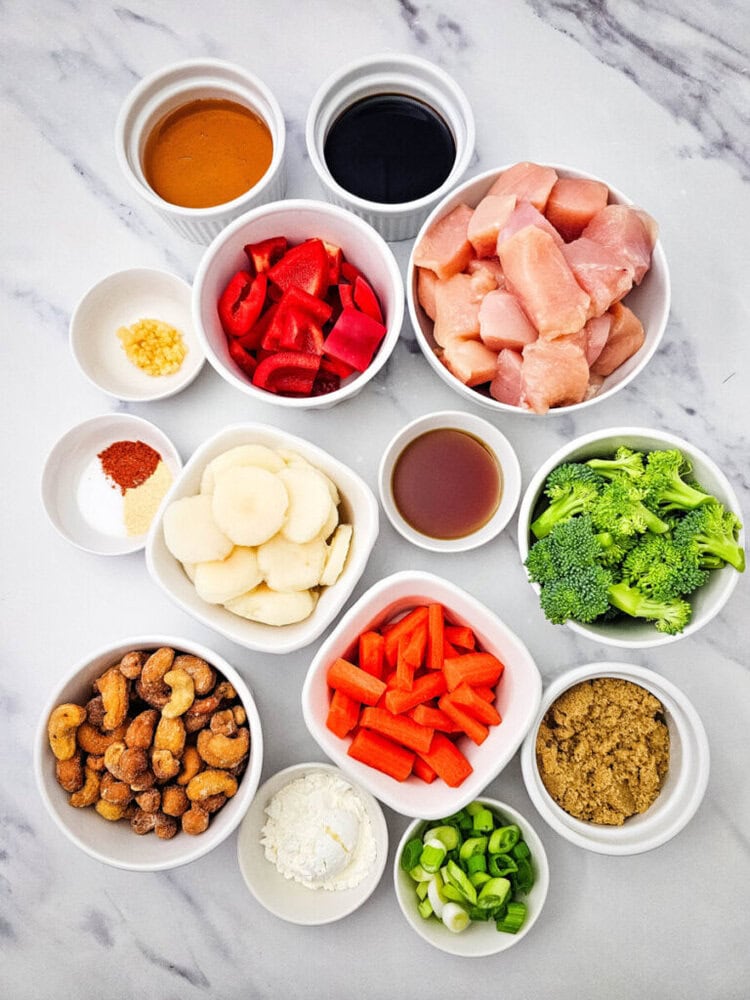 Sheet pan cashew chicken ingredients prepped and arranged in bowls on marble countertop