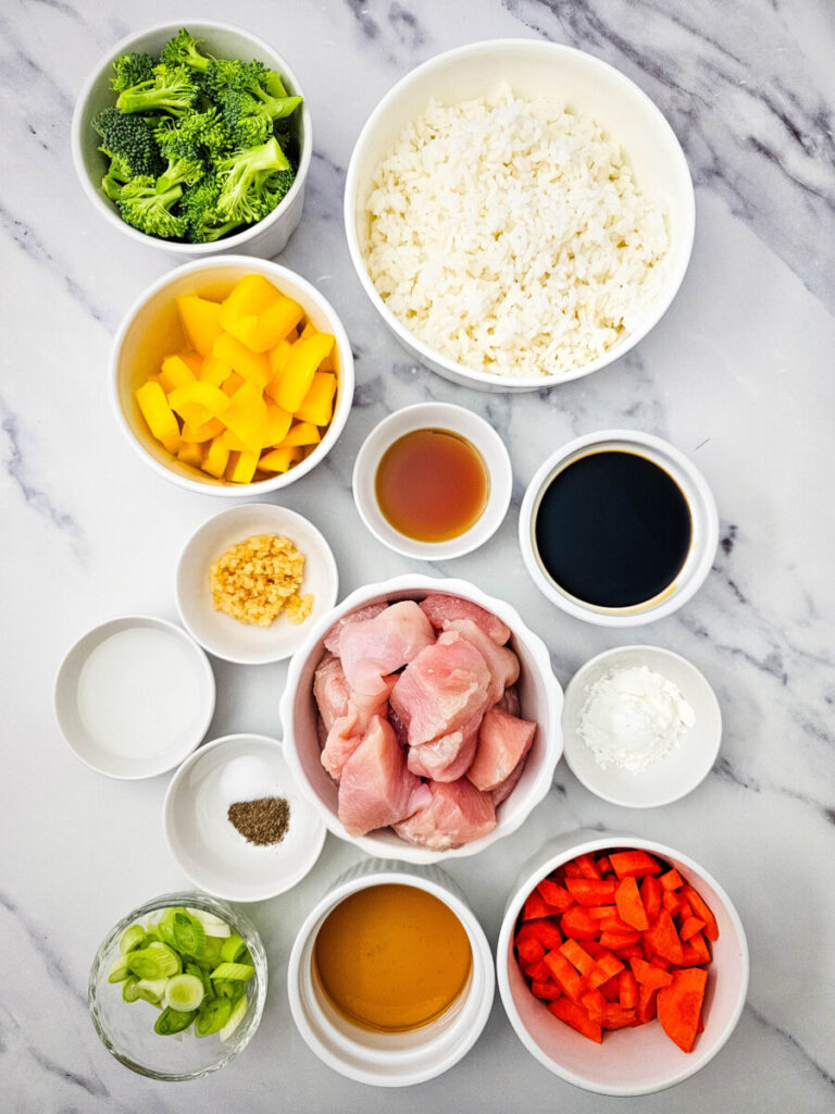 Teriyaki chicken rice bowl ingredients prepped in bowls including raw chicken, rice, vegetables, and soy sauce