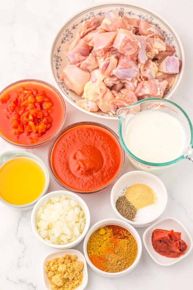 Slow Cooker Chicken Tikka Masala ingredients arranged in bowls including raw chicken, tomato paste, cream, spices, and aromatics