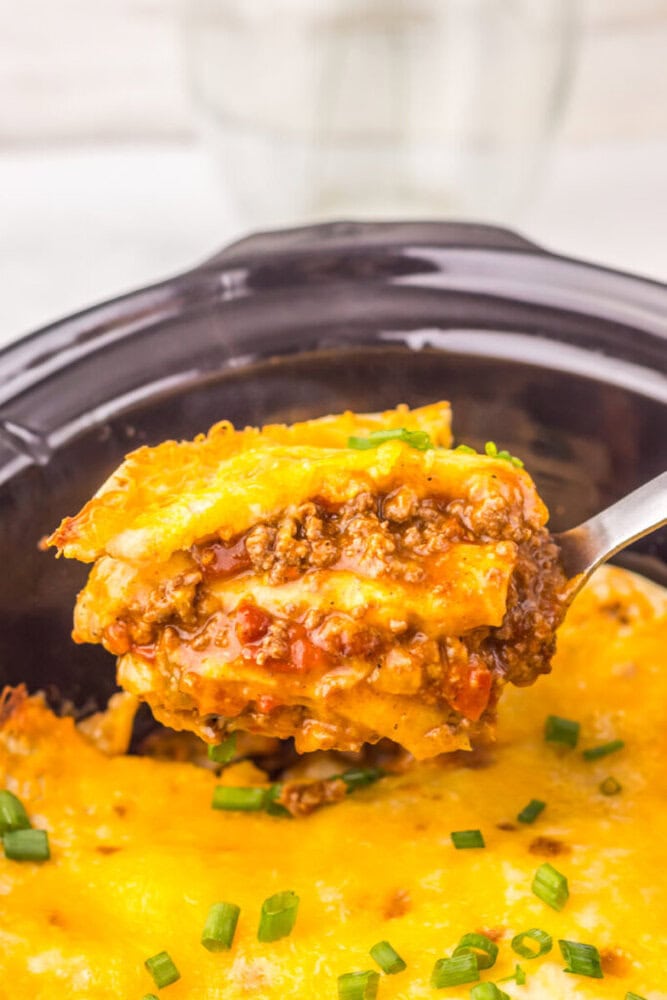 Close-up of slow cooker chili cheese enchilada bake with spoon lifting a serving, showing melted cheese and ground beef filling