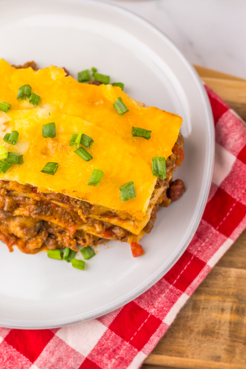 Slow cooker chili cheese enchilada bake with melted cheese and green onion garnish on white plate