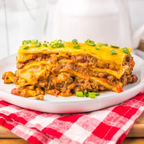 Slow cooker chili cheese enchilada bake with melted cheddar and green onions on white plate