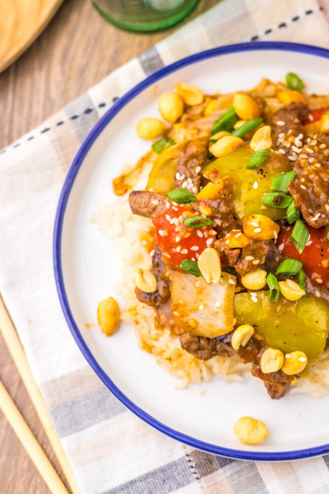 Slow cooker Kung Pao beef with corn and sesame seeds served over rice on a white plate