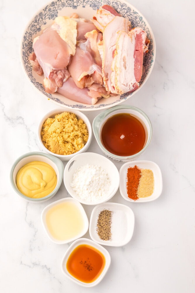 Slow cooker maple bacon chicken ingredients laid out including raw chicken, bacon, maple syrup, mustard, and spices in small bowls