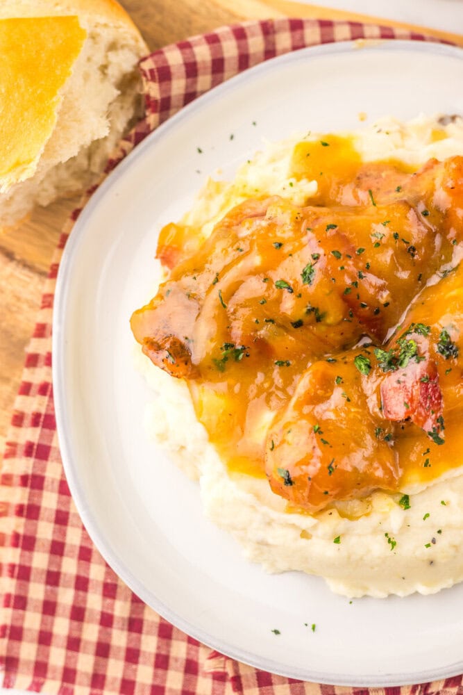 Slow cooker maple bacon chicken with glazed bacon pieces over mashed potatoes, garnished with parsley