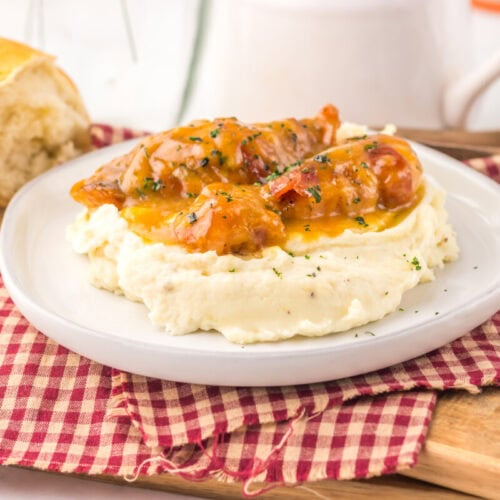 Slow cooker maple bacon chicken served over mashed potatoes with herb garnish on white plate