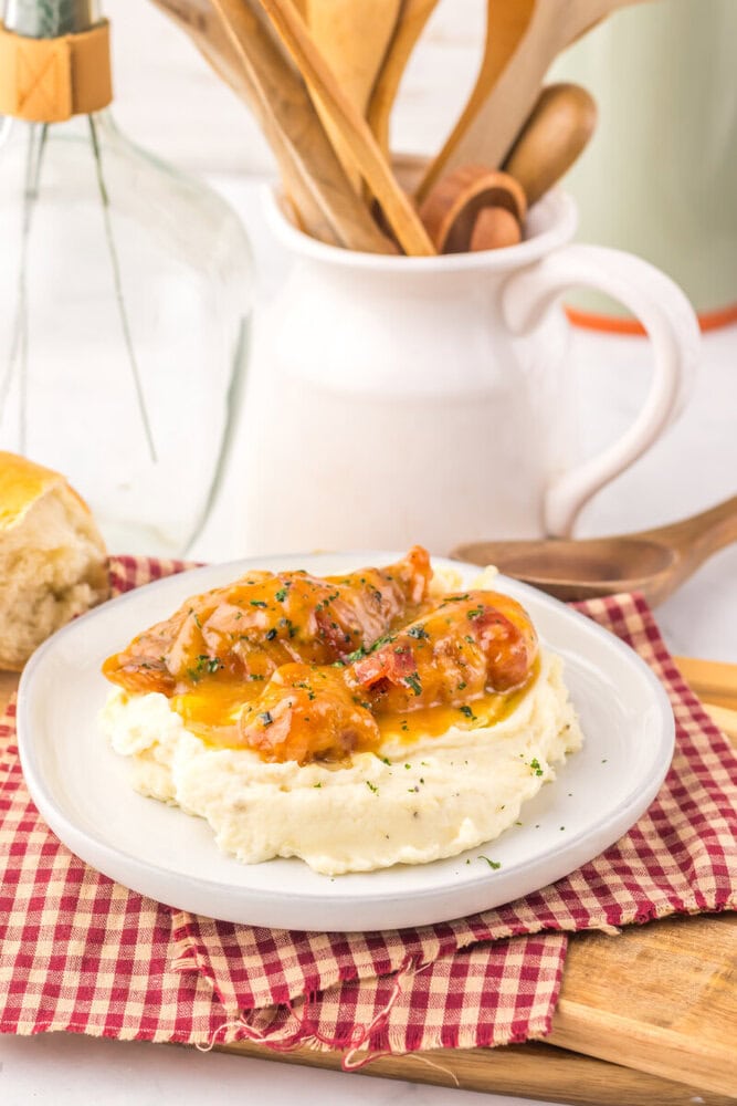Slow cooker maple bacon chicken with mashed potatoes on white plate, garnished with herbs