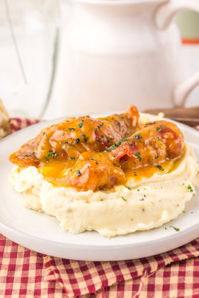 Slow cooker maple bacon chicken with glazed sauce served over creamy mashed potatoes, garnished with fresh thyme