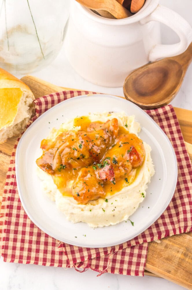 Slow cooker maple bacon chicken with mashed potatoes, garnished with herbs on a white plate with wine and bread