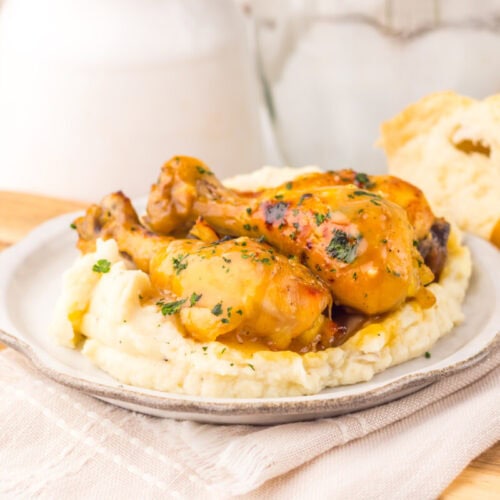 Slow cooker maple Dijon chicken legs served over mashed potatoes with fresh herb garnish