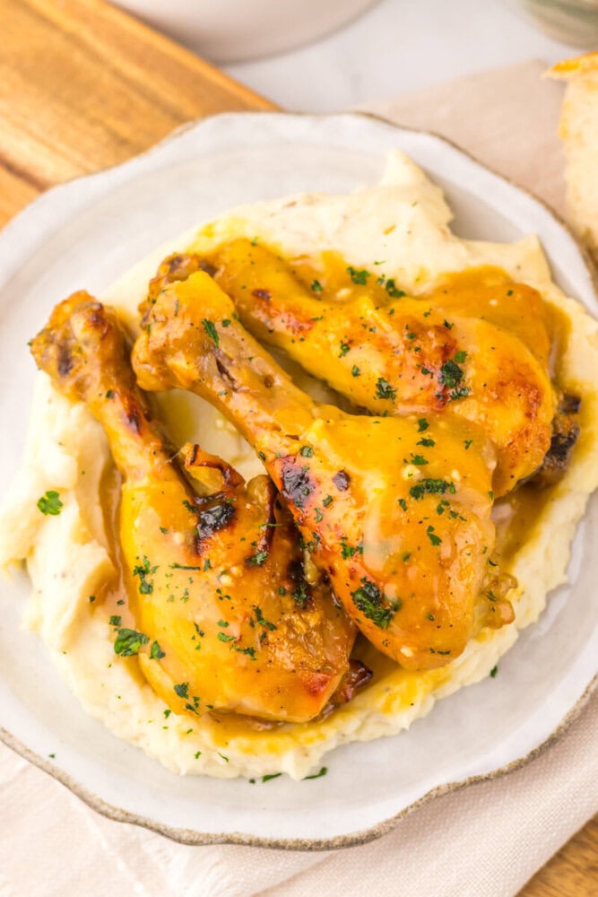 Slow cooker maple Dijon chicken legs plated on mashed potatoes with parsley garnish