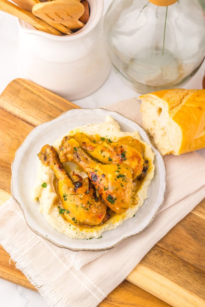Slow cooker maple Dijon chicken leg served over mashed potatoes with fresh bread and herbs