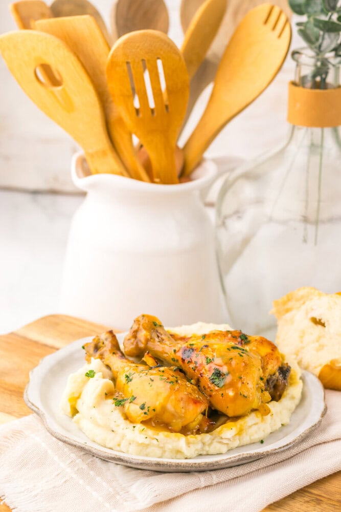 Slow cooker maple Dijon chicken legs served on mashed potatoes with herb garnish