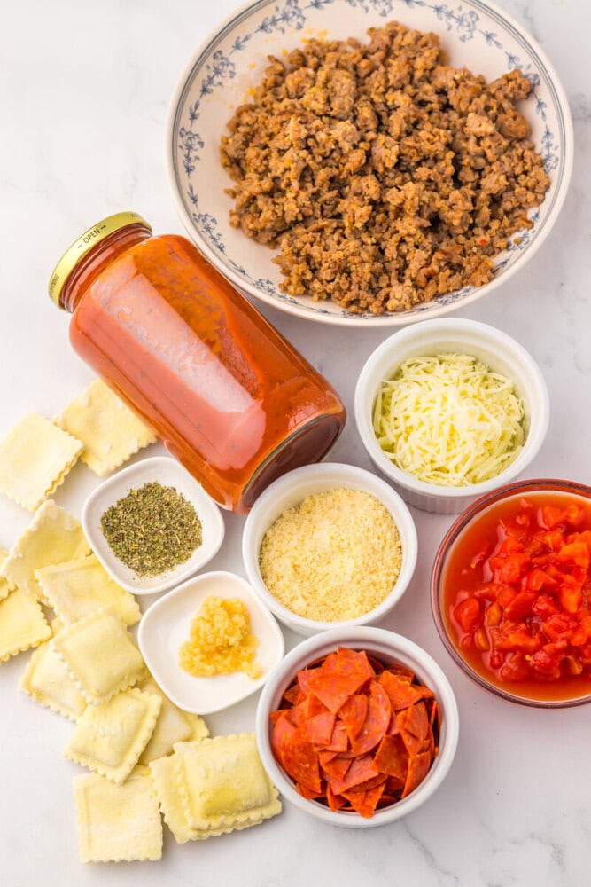 slow cooker pizza ravioli ingredients arranged overhead - ground meat, ravioli pasta, marinara sauce, cheese, pepperoni, and seasonings in bowls