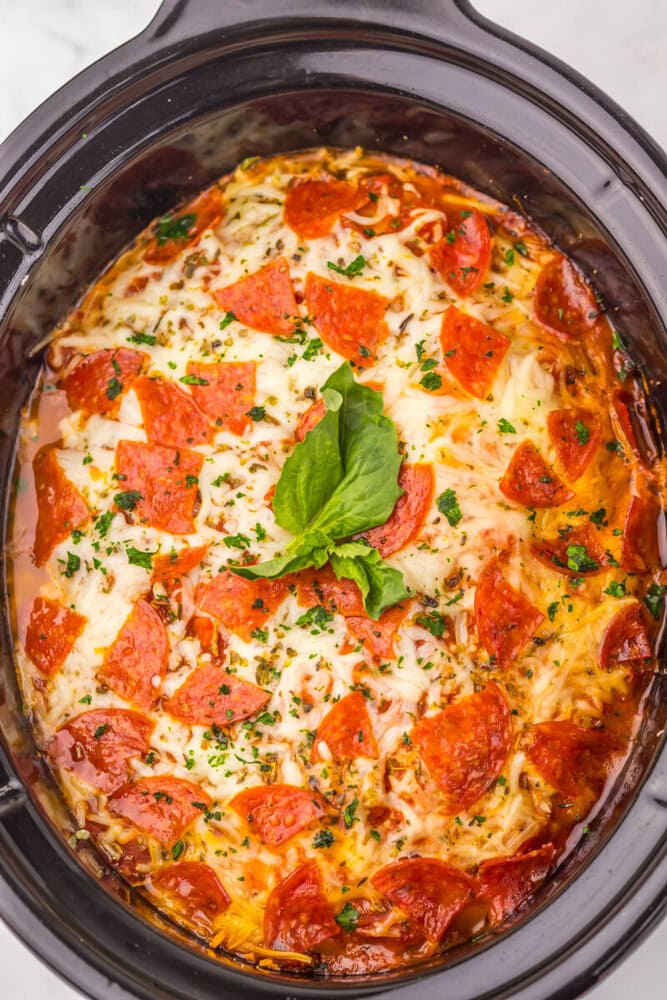 Slow cooker pizza ravioli with pepperoni, melted cheese, and fresh basil in an oval slow cooker