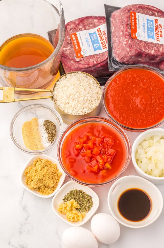 Slow cooker porcupine meatballs ingredients laid out including ground beef, rice, tomato sauce, broth, bell peppers, onions, and seasonings