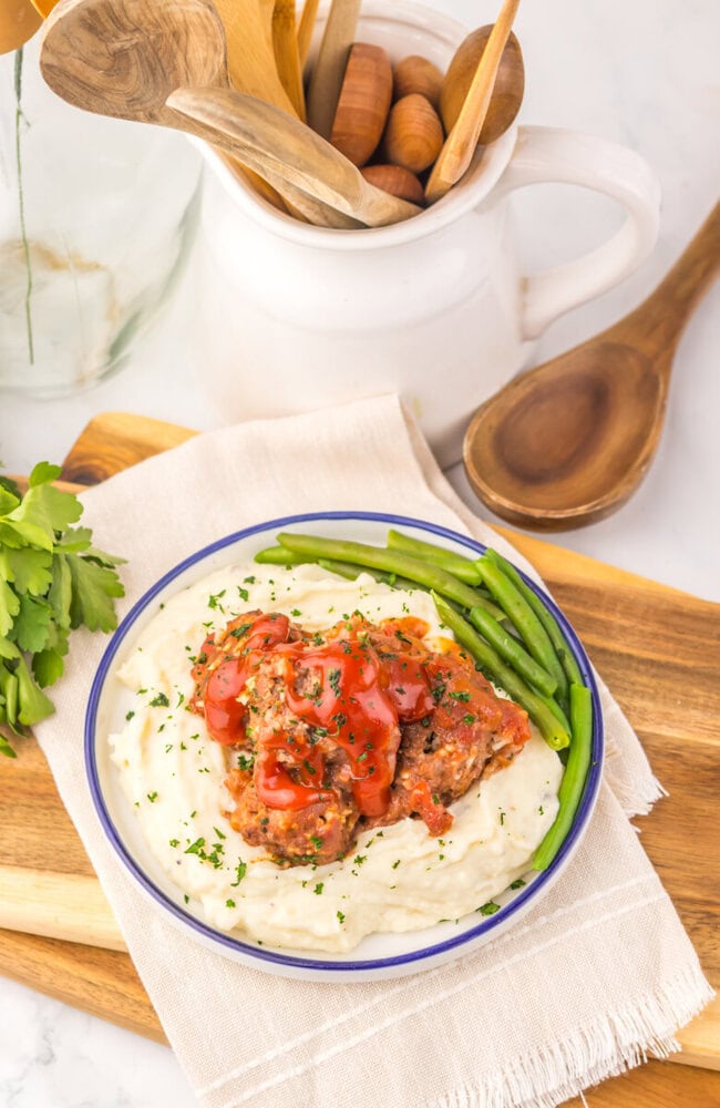 Slow cooker porcupine meatballs plated on creamy mashed potatoes with green beans and tomato garnish