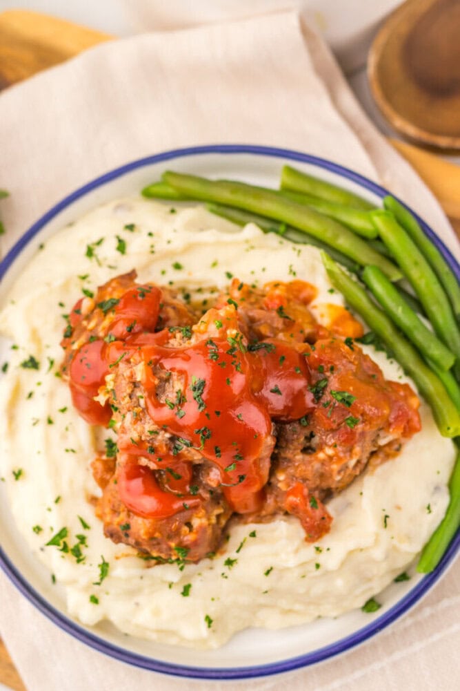 Slow cooker porcupine meatballs served on mashed potatoes with green beans and fresh parsley garnish