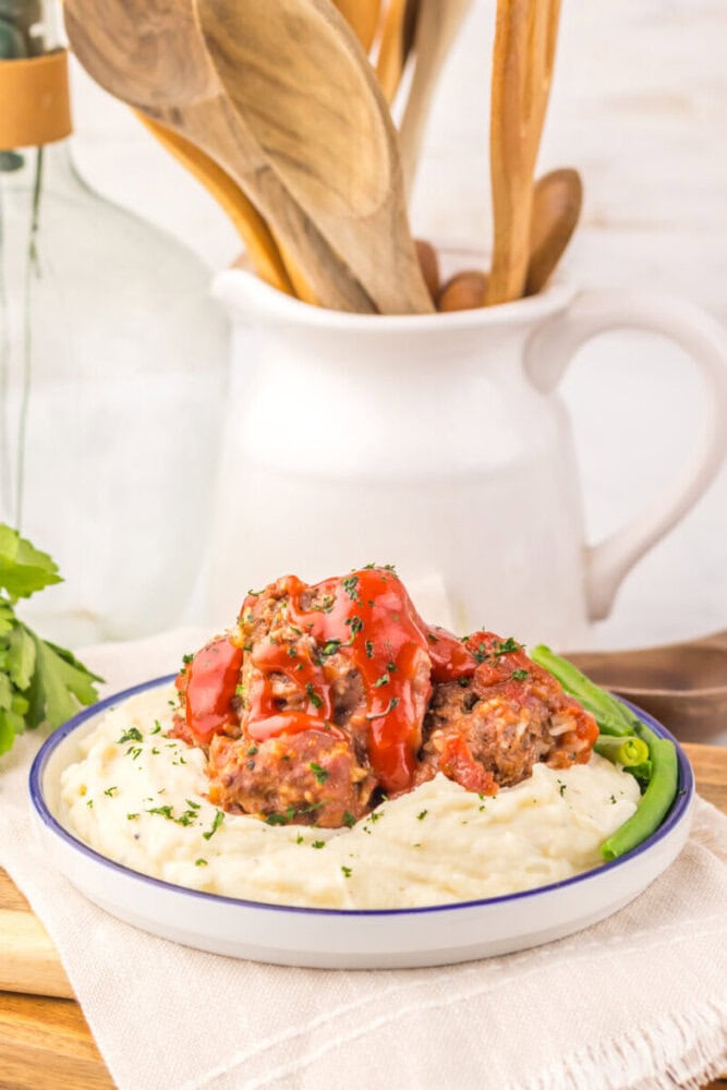 Slow cooker porcupine meatballs served on mashed potatoes with tomato sauce and fresh parsley garnish