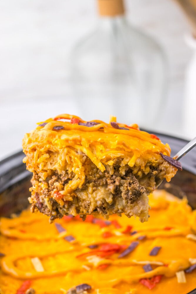 Slow cooker taco bell grilled cheese burrito casserole with melted cheddar cheese and ground beef being served with a spoon