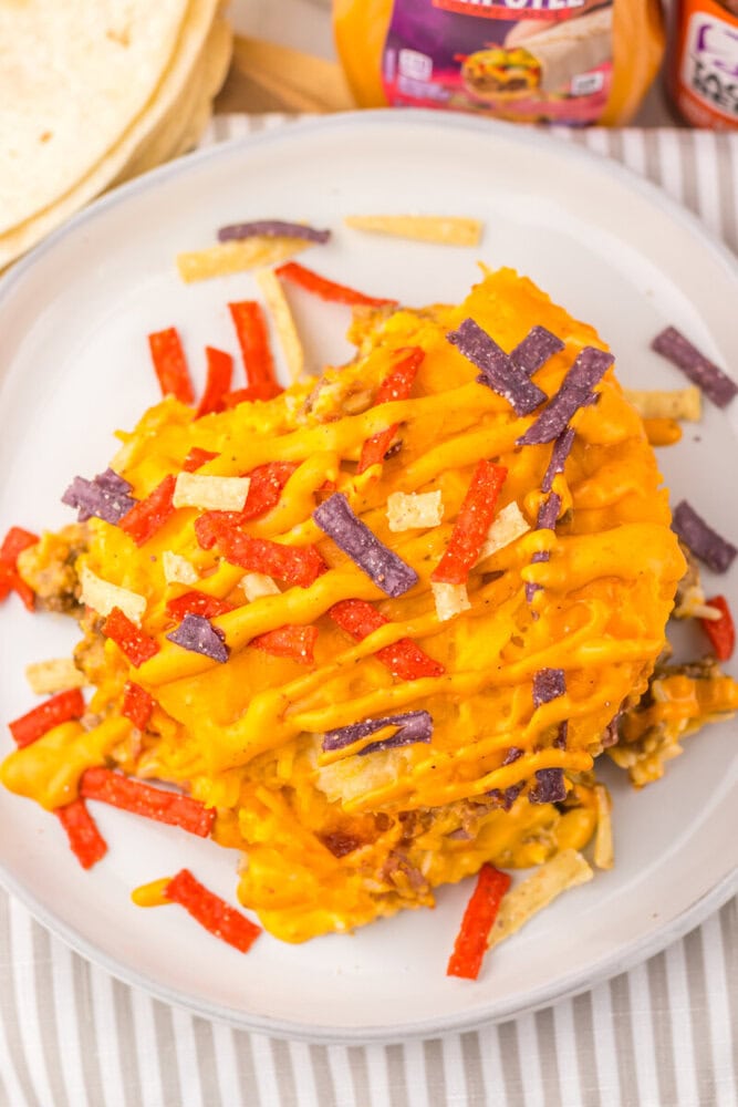 Slow cooker taco bell grilled cheese burrito casserole topped with melted cheese and colorful toppings on a white plate