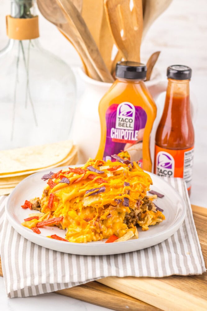 Slow Cooker Taco Bell Copycat Grilled Cheese Burrito Casserole plated with cheese and bacon, styled with Taco Bell Chipotle sauce