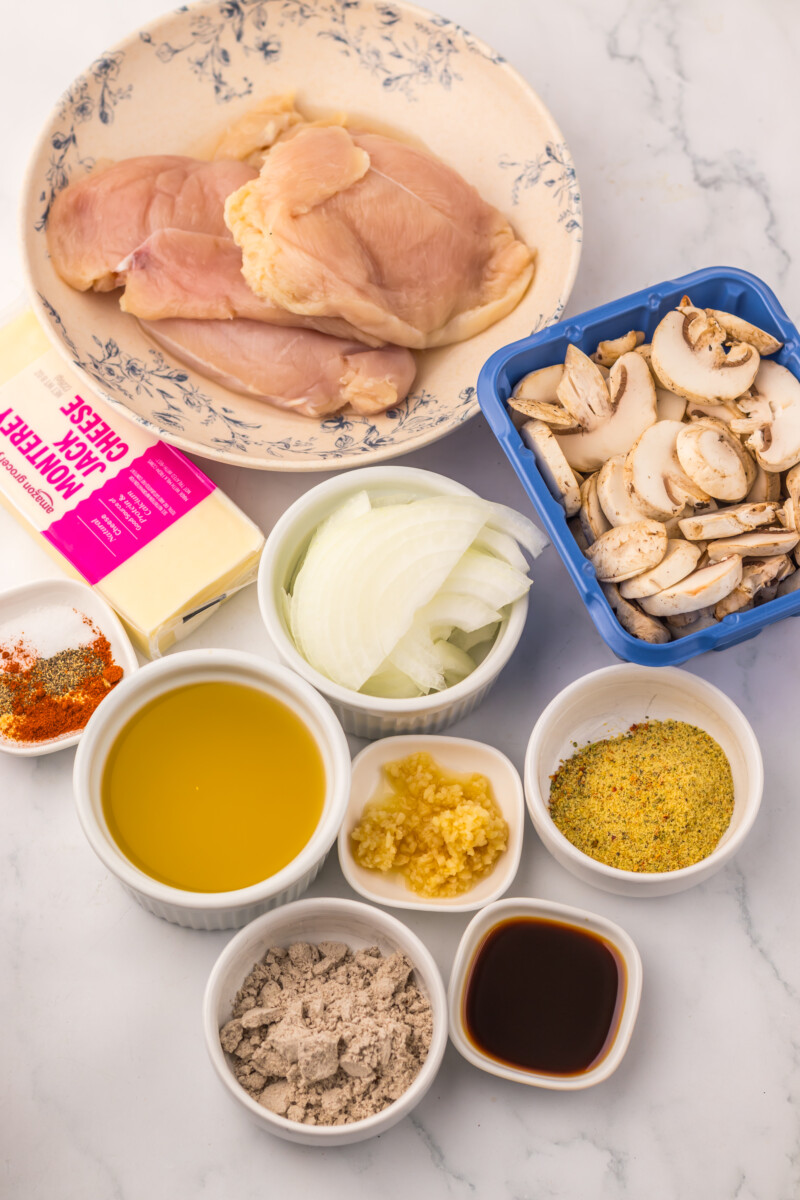 Slow cooker smothered chicken ingredients including raw chicken, mushrooms, onions, olive oil, and seasonings arranged overhead on marble