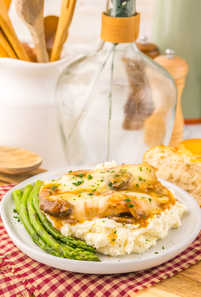 Slow cooker smothered chicken with melted cheese and mushrooms over creamy mashed potatoes and asparagus