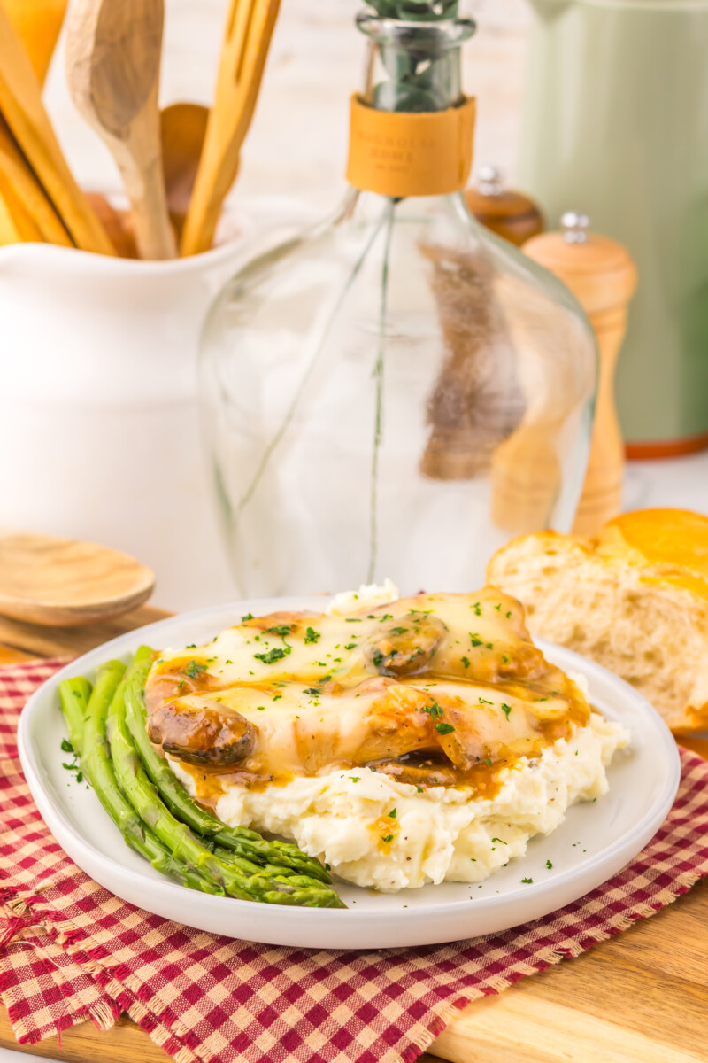 Slow cooker smothered chicken with melted cheese and mushrooms served with asparagus on white plate