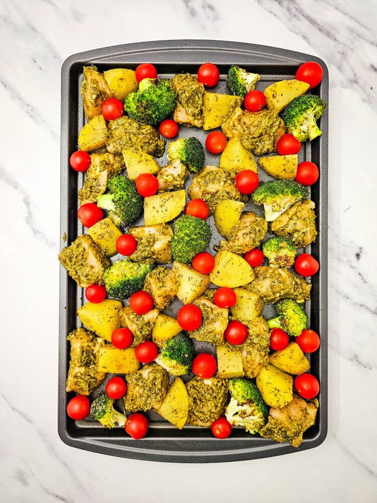 Sheet pan pesto chicken with roasted potatoes, broccoli, and tomatoes on marble background