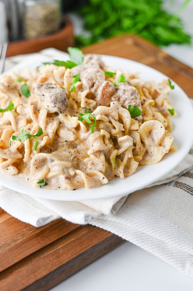 Slow cooker creamy beef and noodles served on white plate with green onion garnish