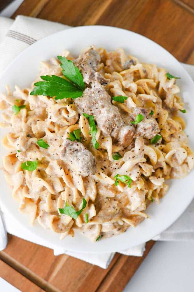 Slow cooker creamy beef and noodles with parsley garnish on white plate
