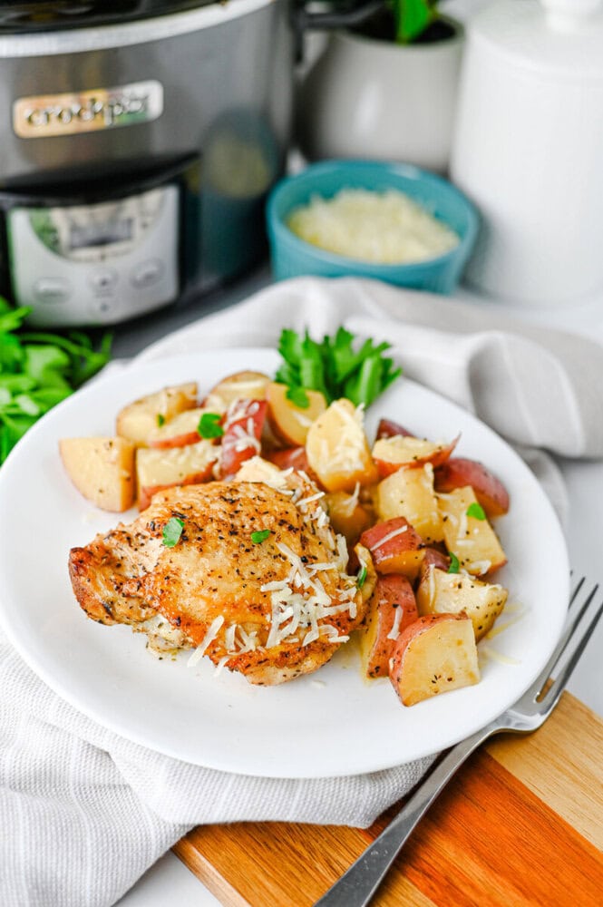 Slow cooker garlic parmesan chicken and potatoes plated on white dish with fresh parsley garnish
