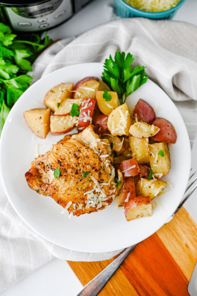 Slow cooker garlic Parmesan chicken and potatoes plated on white dish with fresh parsley garnish