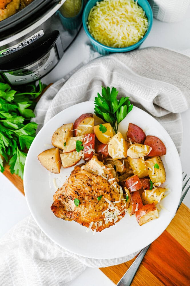 Slow cooker garlic Parmesan chicken and potatoes plated with fresh parsley garnish and Parmesan cheese