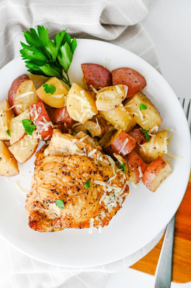 Slow cooker garlic parmesan chicken and potatoes plated on white dish with parmesan cheese and fresh parsley garnish