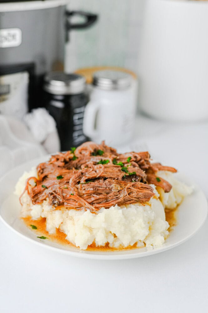 Slow Cooker Mississippi Pot Roast with shredded beef on creamy mashed potatoes garnished with green onions