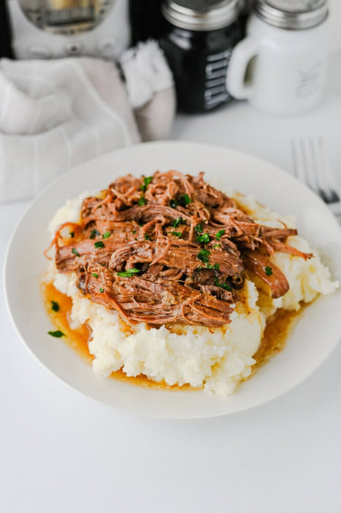 Slow Cooker Mississippi Pot Roast with shredded beef and peppers served over mashed potatoes, garnished with parsley