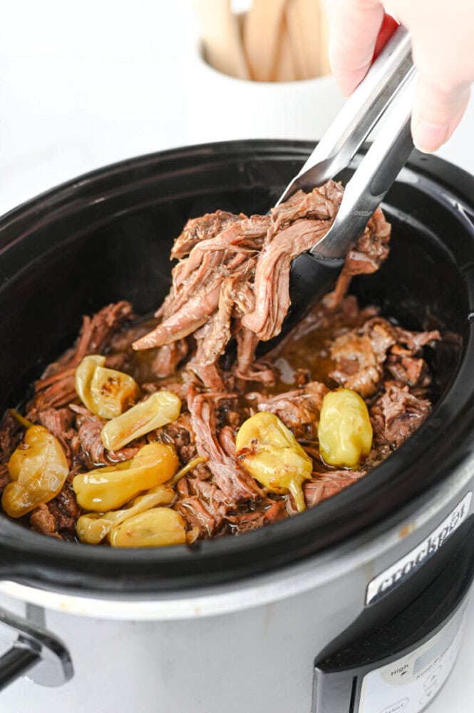 Slow cooker mississippi pot roast with shredded beef and pepperoncini peppers being served with tongs