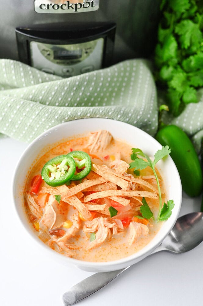 Slow cooker creamy chicken enchilada soup in white bowl with jalapeño and cilantro garnish