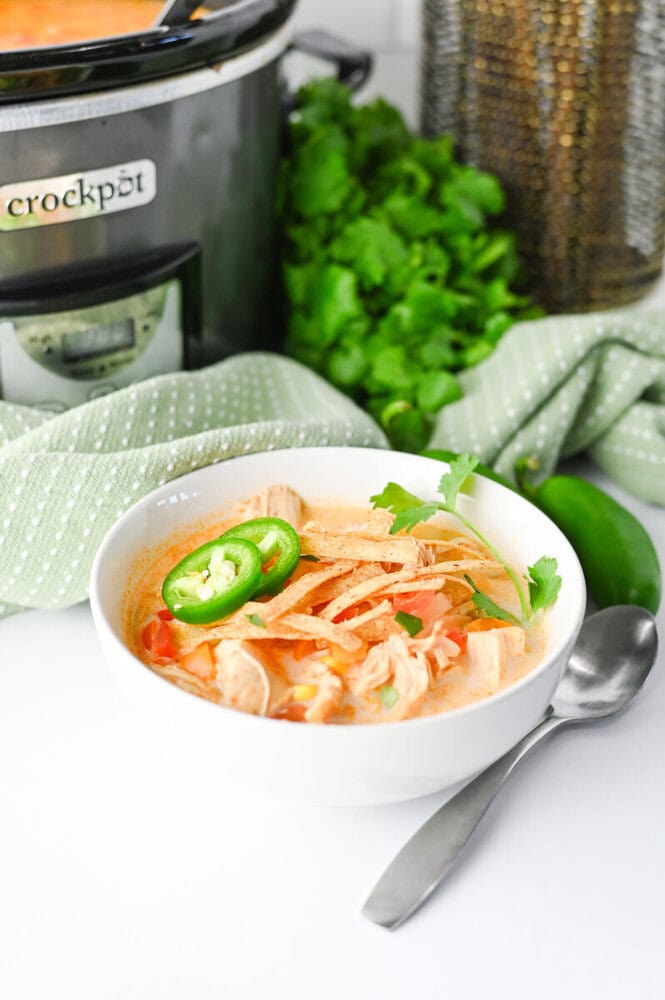 Slow cooker creamy chicken enchilada soup in white bowl with jalapeño and cilantro garnish