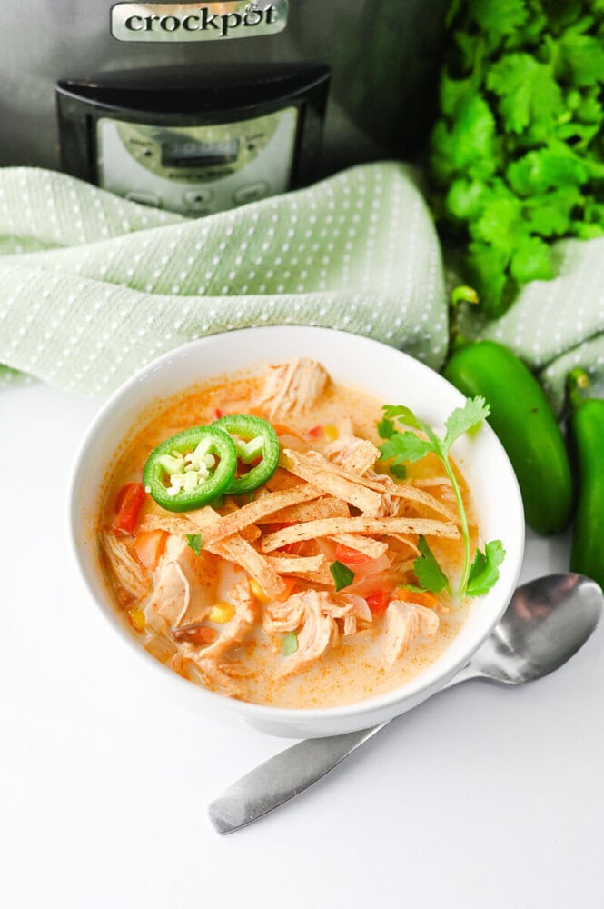 Slow cooker creamy chicken enchilada soup in white bowl garnished with jalapeños and cilantro